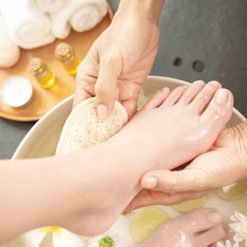 foot washing in spa before treatment. spa treatment and product for female feet and hand spa. white flowers in ceramic bowl with water for aroma therapy at spa.